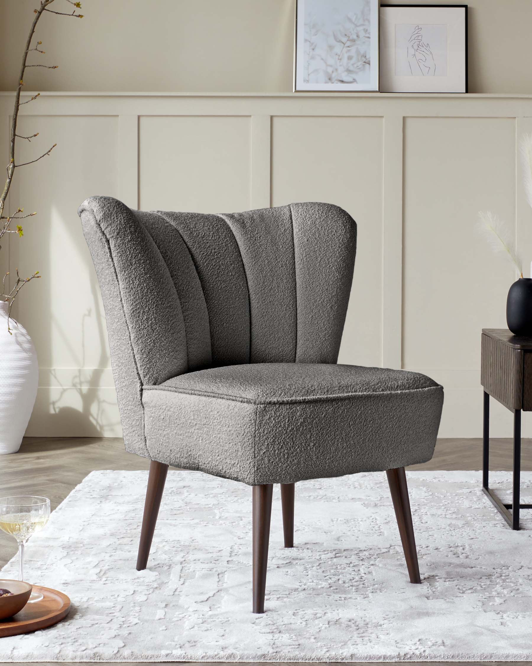 Modern upholstered wingback accent chair with textured fabric, angled wooden legs, and a curved backrest, set in a stylish room with decorative panelling and minimalistic art.