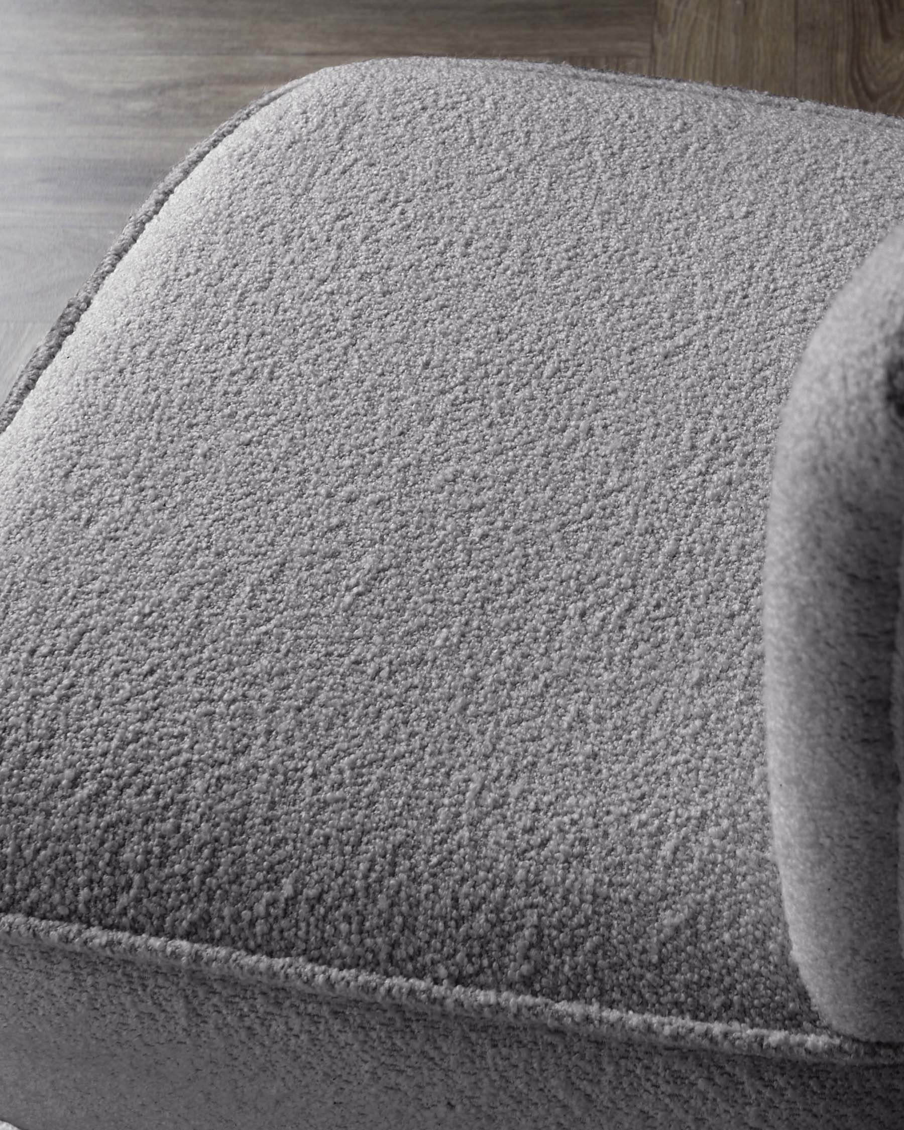 Close-up view of a textured grey fabric upholstered furniture piece, possibly a sofa or armchair, with a focus on the plush and comfortable cushioning.