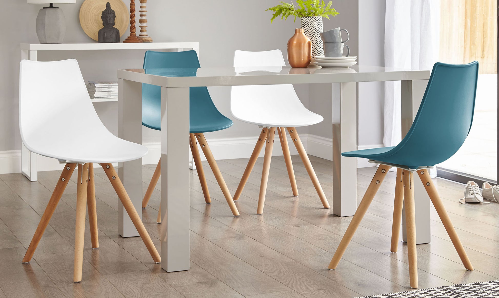 Modern dining set featuring a rectangular white table with sleek straight legs paired with four scoop-back chairs, two in white and two in teal, all with light wooden splayed legs connected by metal brackets.