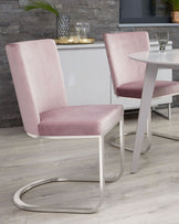 Modern dining room with blush pink velvet chairs featuring a unique, curved brushed metal base and a round white table with a matching brushed metal stand.