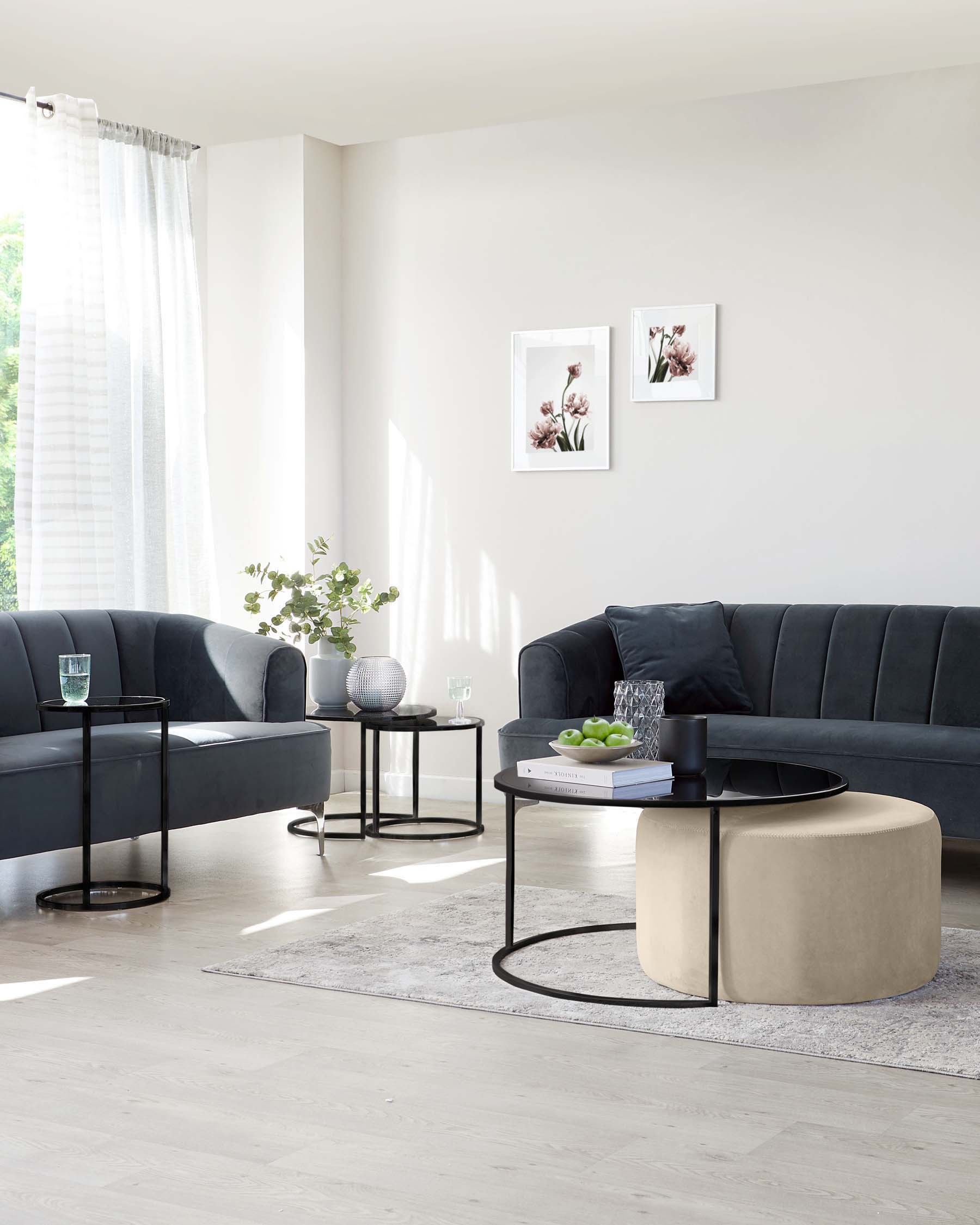 Elegant living room setup featuring a plush dark grey sectional sofa with a tufted backrest, a round beige ottoman with a black tray on top, two circular black metal side tables with glass tops, and a rectangular rug with a muted pattern underfoot.