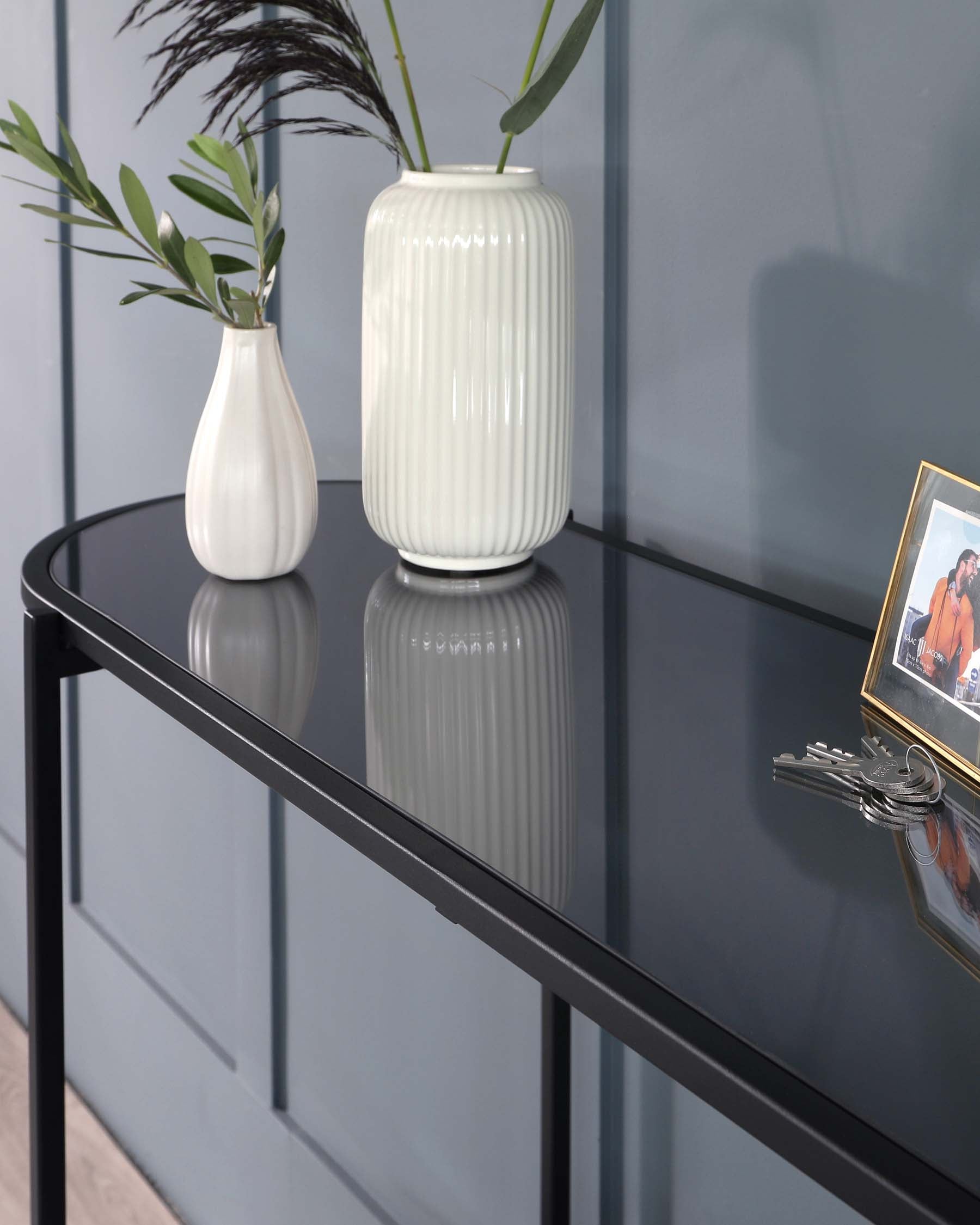 Modern minimalist black metal console table with a reflective glass top, displaying decorative items.