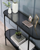 A modern two-tiered console table featuring a sleek black metal frame with semi-circular supports and glossy black glass shelves.