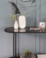 A modern, oval-shaped, black console table with a glossy finish and slender, straight metal legs.