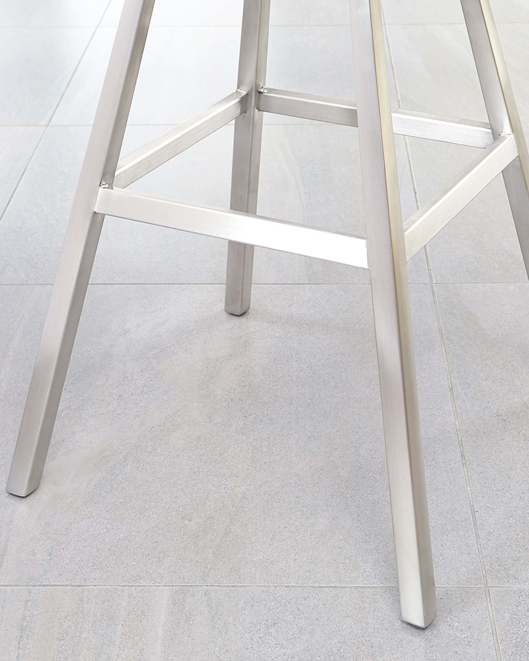 Close-up of a modern metallic table leg with a crossbar, showcasing minimalistic and sleek design on a light grey tiled floor.