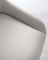 Close-up of a modern light grey leather chair with a smooth, curved silhouette and fine stitching details, set against a white wooden floor backdrop.