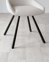 Modern minimalist chair with a curved, off-white upholstered seat and a set of four splayed, black metal legs, displayed on light wood flooring.