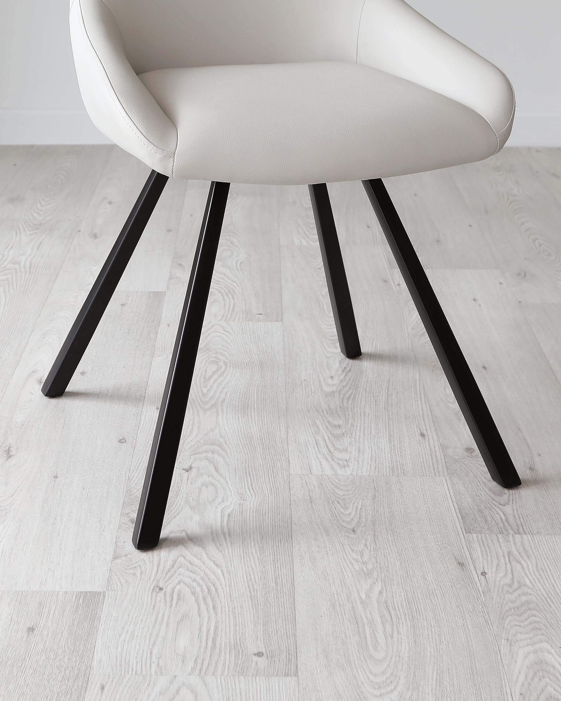 Modern minimalist chair with a curved, off-white upholstered seat and a set of four splayed, black metal legs, displayed on light wood flooring.