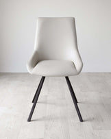 Modern light beige upholstered dining chair with a cushioned seat and backrest, featuring a curved silhouette and dark angular metal legs, set on a light wooden floor against a white wall.