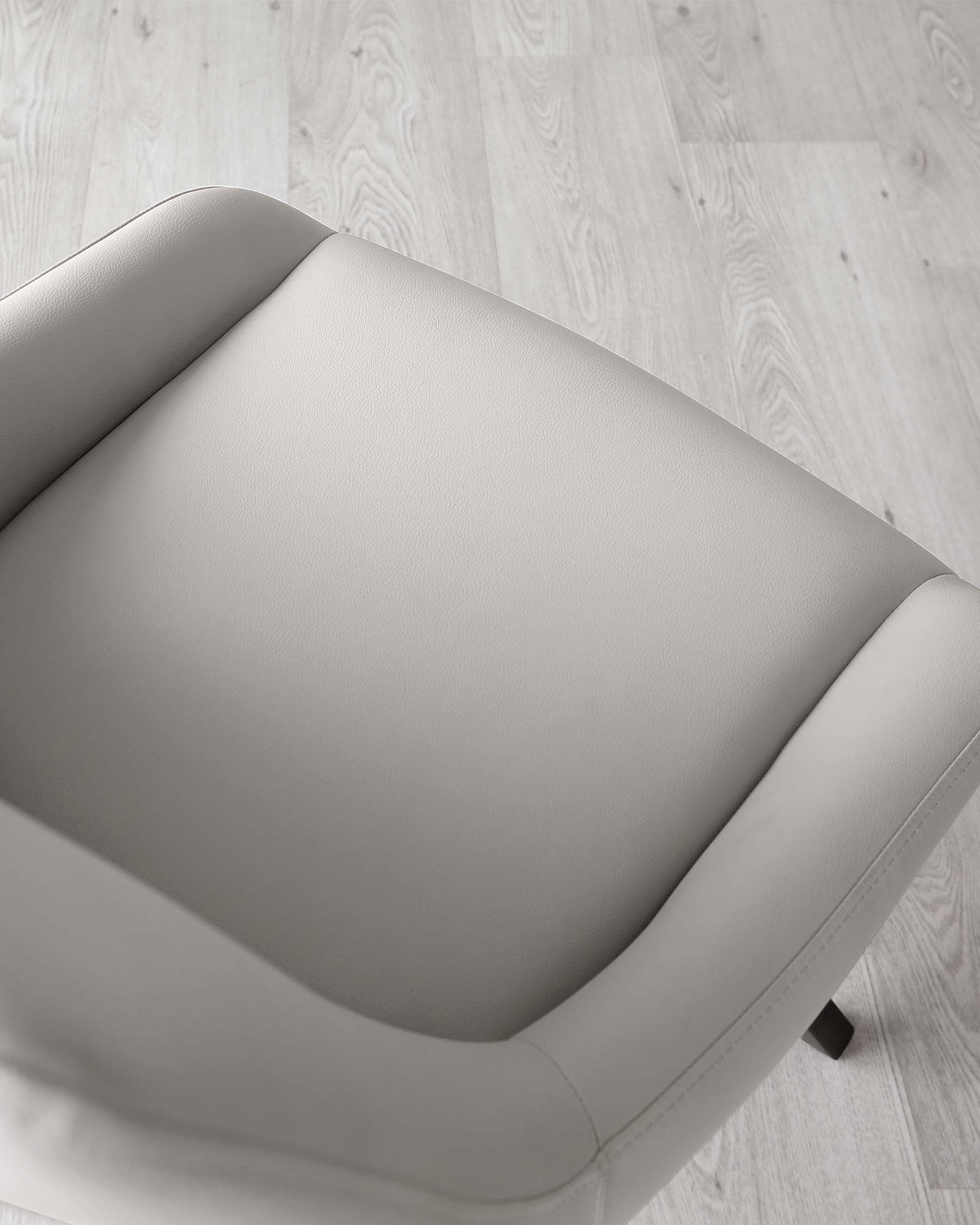 Modern light grey armchair with a wide, cushioned seat and gently sloping armrests, featuring a smooth, leather-like upholstery on a light wooden floor.