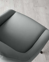 Modern minimalist armchair with a sleek, grey upholstery and angled wooden legs on a light wooden floor.