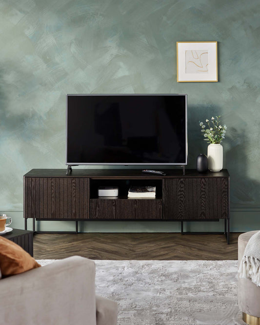 Modern TV stand with a dark wood finish, sleek lines, open shelving, and decorative vases placed on top, set against a green wall.