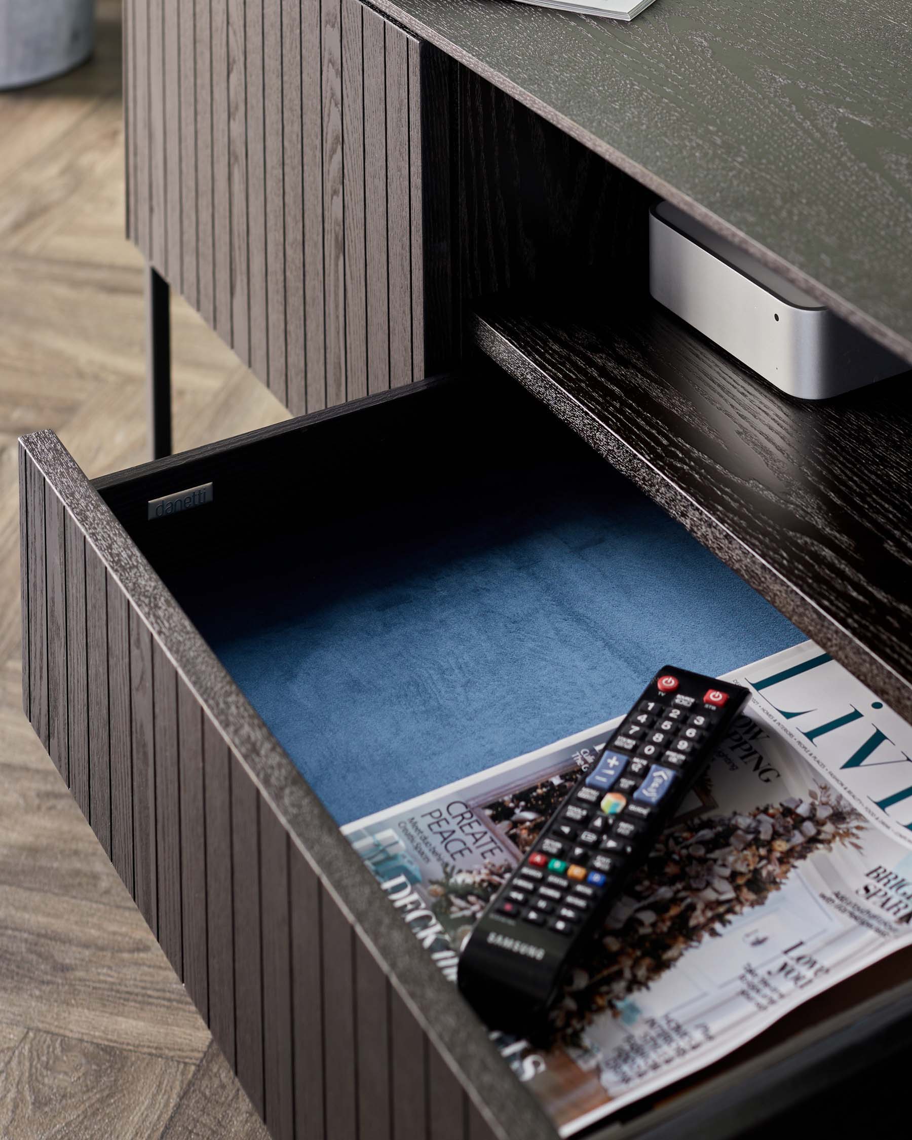 Stylish dark wood drawer unit with textured finish, featuring a blue interior, magazines, and a remote control on display.