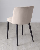 Modern minimalist chair with beige upholstery and black metal legs on a light wooden floor against a grey background.