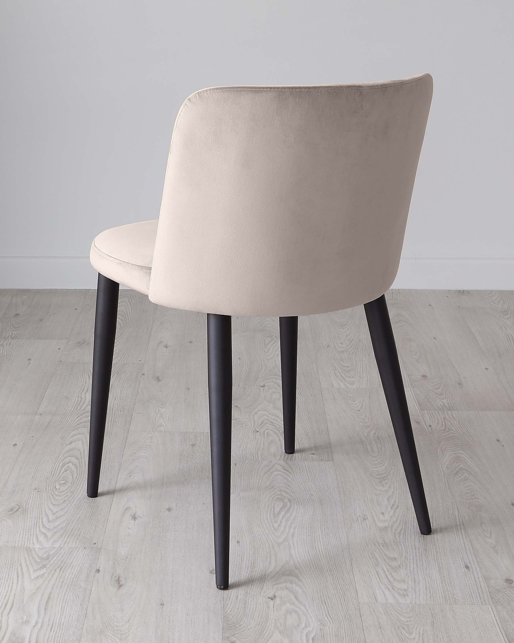 Modern minimalist chair with beige upholstery and black metal legs on a light wooden floor against a grey background.