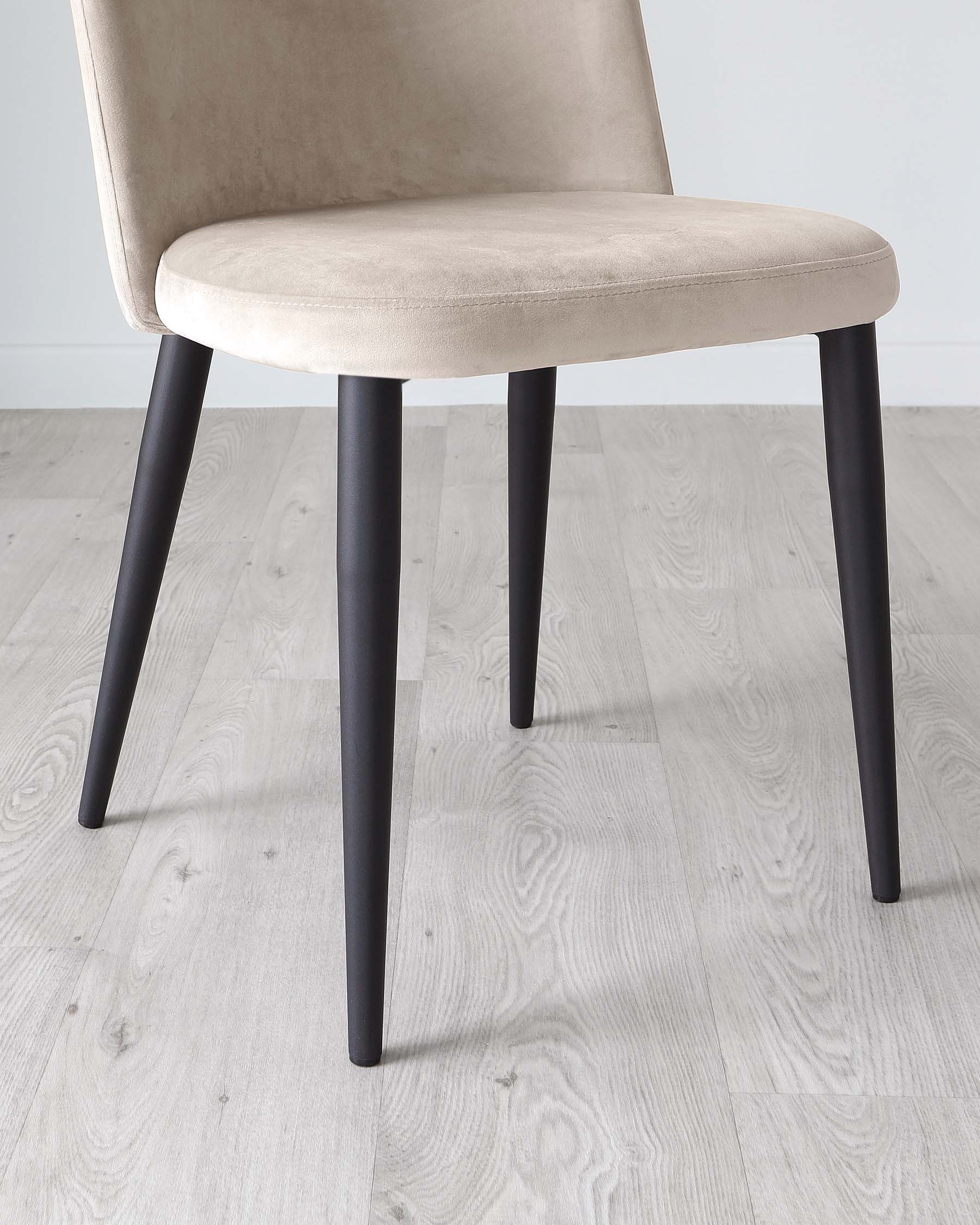 Modern dining chair with a beige upholstered seat and backrest, featuring clean lines and contrasting dark tapered wooden legs. The neutral colour scheme makes it versatile for various dining room decors.