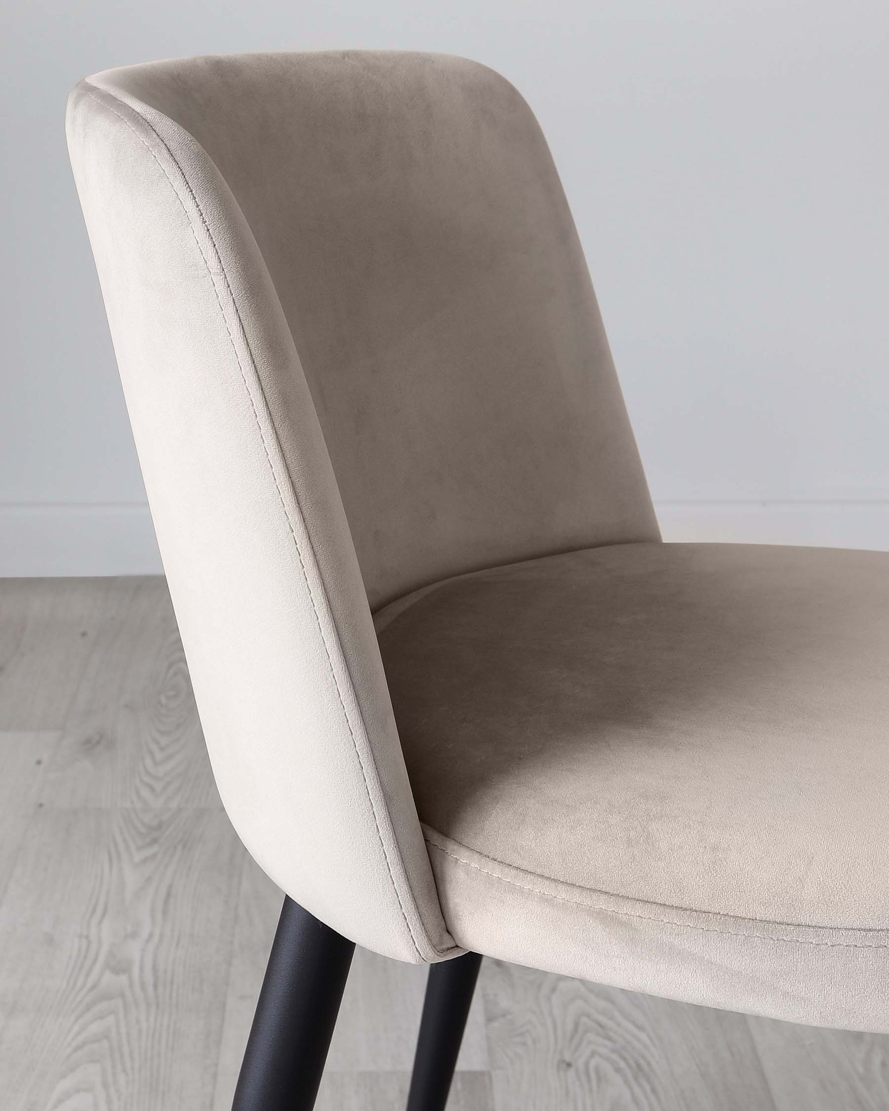 A contemporary dining chair featuring a curved backrest and cushioned seat with light beige upholstery. The chair has visible stitching details along the edges and is supported by tapered black metal legs. The design offers a blend of modern minimalism and comfort.