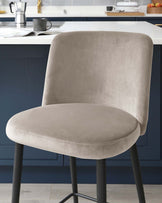 Elegant modern velvet dining chair with a curved backrest and a cushioned seat, featuring sleek, black metal legs. The chair's luxurious light grey upholstery provides a smooth, soft texture, ideal for contemporary interior designs.