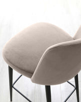 Modern minimalist chair with a curved beige upholstered seat and backrest, complemented by sleek black metal legs, photographed on a light wood floor against a bright background.