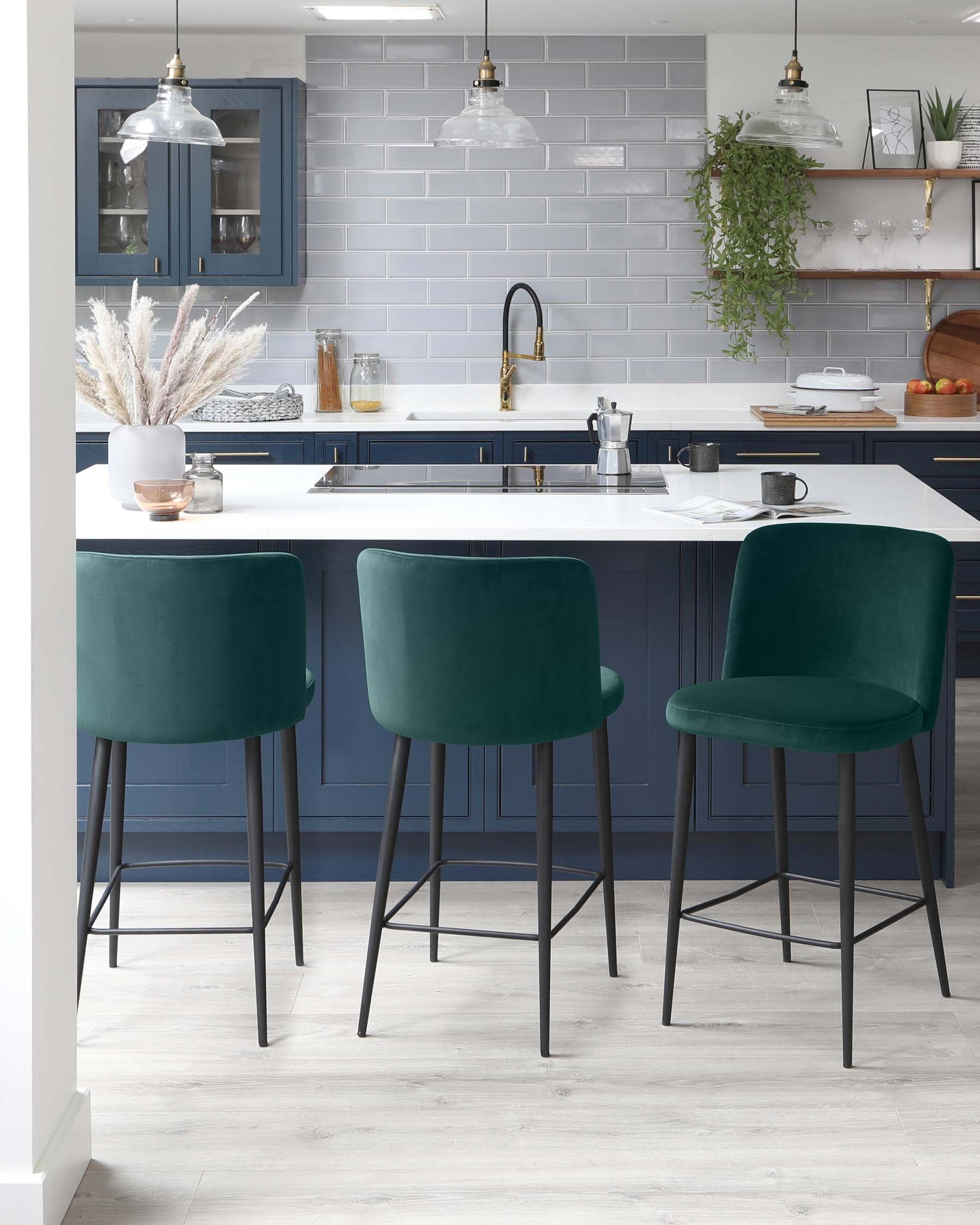 Three contemporary dark teal upholstered bar stools with black metal legs positioned at a kitchen island.