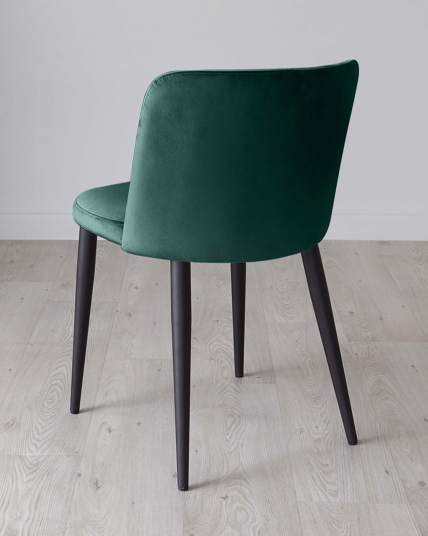 Elegant modern dining chair with a luxurious emerald green velvet upholstery and four straight, slender black metal legs. The chair features a smooth, curved backrest for added comfort, and its sleek design makes it suitable for a variety of dining room styles.