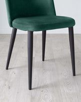 Dark green velvet upholstered chair with a curved backrest and sleek black metal legs, showcased on a light wooden floor.