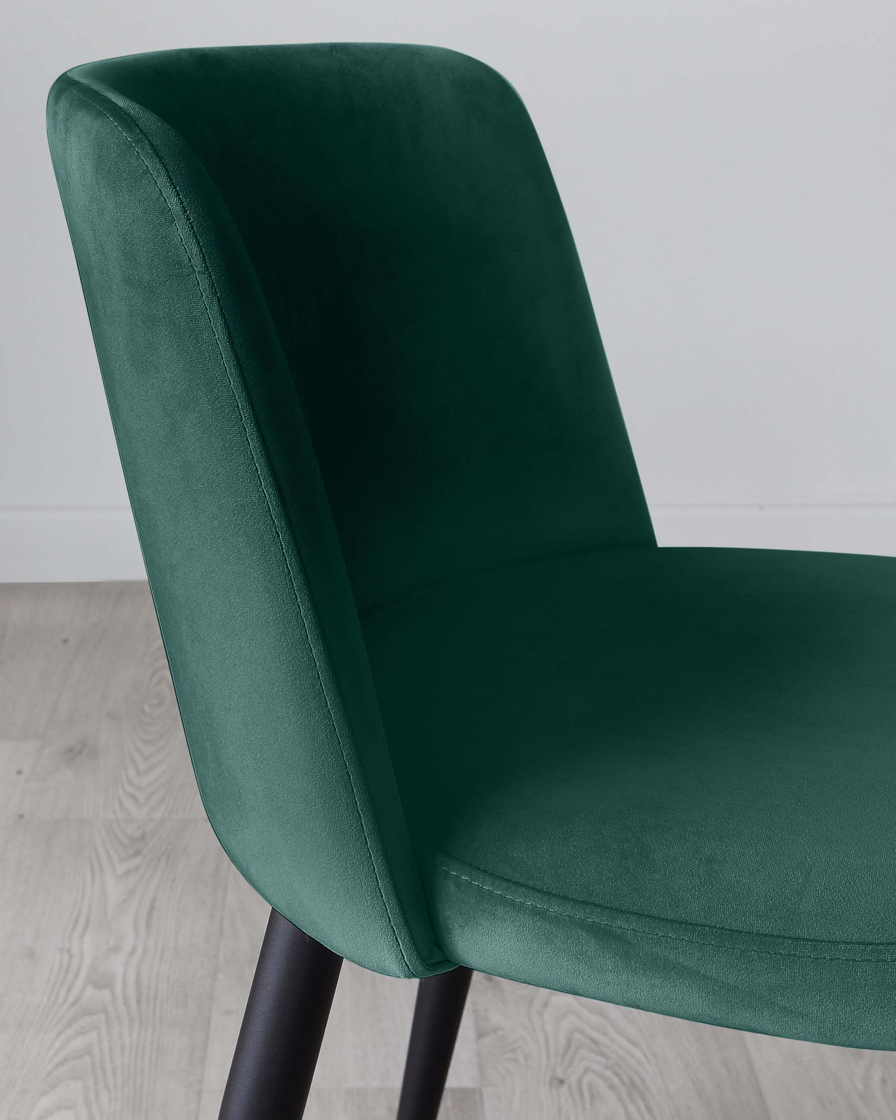 Elegant emerald green velvet dining chair with a gently curved backrest and cushioned seat, mounted on sleek black metal legs.