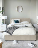 Elegant bedroom furniture including a plush upholstered bed frame with a tufted headboard, clean-lined white nightstands with gold hardware, and matching contemporary white table lamps.