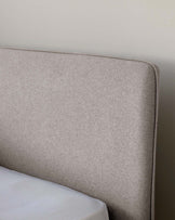 Part of a modern upholstered headboard in light heathered grey fabric with a gently curved top and clean lines, suggestive of a contemporary bedroom setting.