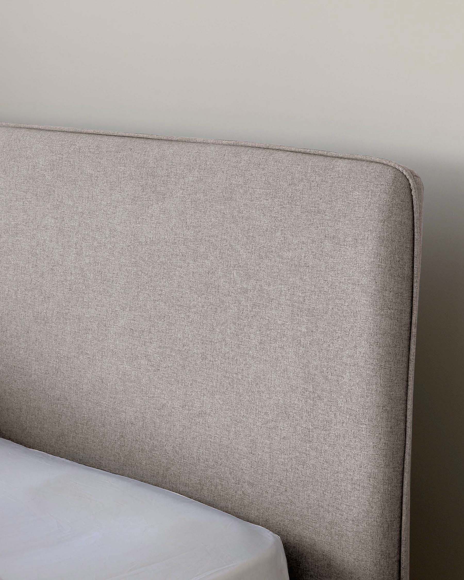 Part of a modern upholstered headboard in light heathered grey fabric with a gently curved top and clean lines, suggestive of a contemporary bedroom setting.