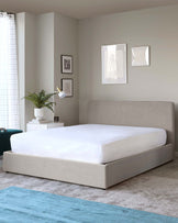 A modern minimalist style upholstered platform bed in a neutral beige fabric with a simple, streamlined headboard and a low-profile design. The bed is dressed with crisp white bedding.