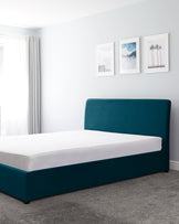 Modern minimalist style platform bed with a teal upholstered headboard and frame, showcased in a clean bedroom with light grey carpet flooring. The bed is neatly covered with a white fitted sheet.