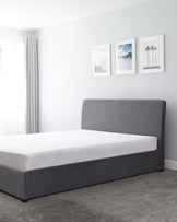 Contemporary-style grey upholstered bed frame with headboard and white bedding, situated in a minimalist bedroom setting.