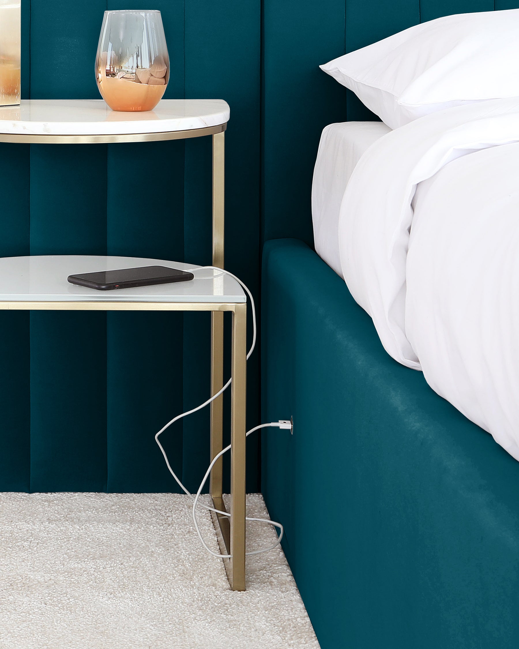 Elegant contemporary two-tiered bedside table with a gold metal frame and white marble surfaces, paired with a plush teal upholstered headboard.