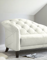 Elegant white tufted sofa with curved arms and dark wooden legs, placed on a soft carpet with a magazine beside it.