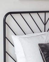 Elegant minimalist black metal headboard with a geometric pattern, paired with crisp white and subtly striped bedding.