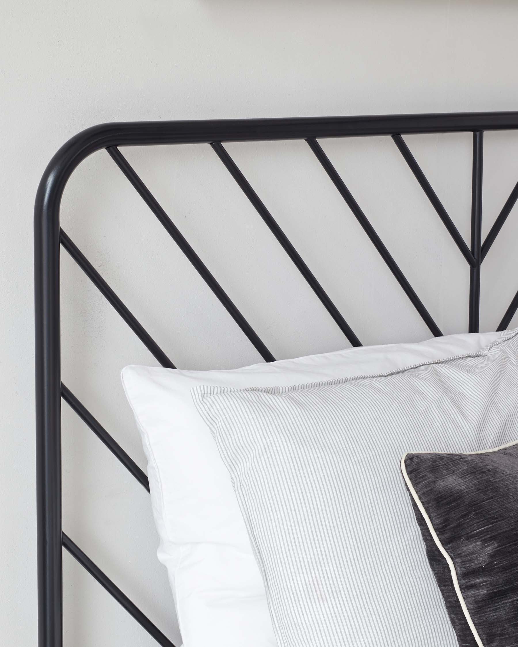 Elegant minimalist black metal headboard with a geometric pattern, paired with crisp white and subtly striped bedding.