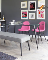 Modern furniture set featuring a sleek glass table with black metal legs, two vibrant fuchsia pink upholstered chairs with black slender legs, and a minimalist light grey padded bench with black slender legs. The ensemble creates a stylish and contemporary look suitable for a chic dining or workspace.