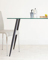 A modern dining setup featuring a clear glass table with angled black legs and a light beige upholstered chair with shiny metal legs.